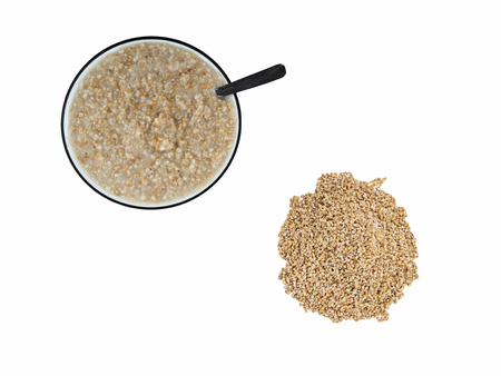 Top view of cooked steel cut oats in bowl next to pile of raw steel cut oats on white backgroundの写真素材