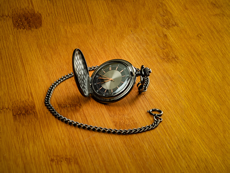 Black opened pocket watch with chain placed on wooden bamboo tableの写真素材