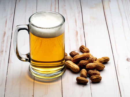 Mug of light beer with peanuts on light wooden tableの写真素材