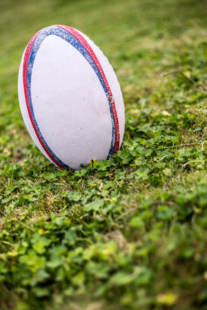 Rugby ball, Gilbert, on sports field with green grass for the game of rugby. Focus on ball, sports base at background.の写真素材