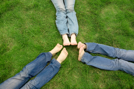 Three girls lying on lawn with foot by footの写真素材