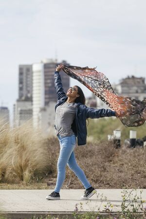 Teenage girl happy with a scarf in the wind with the city in the backgroundの写真素材