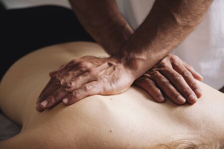 Massage session. Hands massaging on the back with soft light.の写真素材