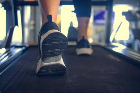 Detail of a person's legs walking on an electric treadmill in a gymnasium wearing trainers and...
