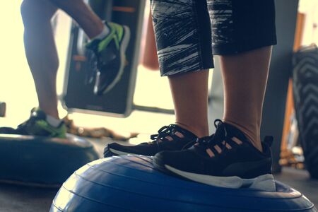 Detail of a person's legs practicing balance on top of a blue medicinal ball in a gymの写真素材