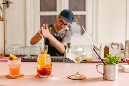 Selective focus in three cocktail glasses prepared with a metal cup with mint on the side at a bar and a waiter with glasses and a cap out of focus on the backgroundの写真素材
