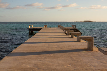 Paved pier entering the sea with calm water on a sunny day and a platform built in the middle of the...