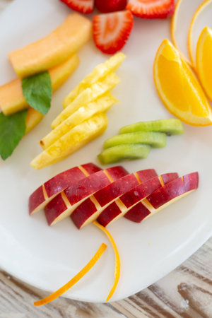 Vertical photo of a white plate with fruit salad cut and separated by flavors in a plate with...