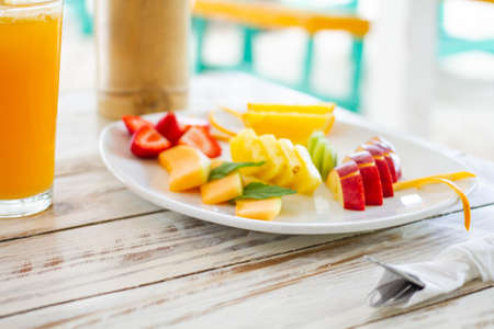 Plate with chopped fruit salad served on a wooden table with orange juice on the sideの写真素材