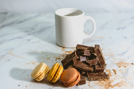 Tasty sweet macarons with cup of coffee on chocolate background and mountain on white background