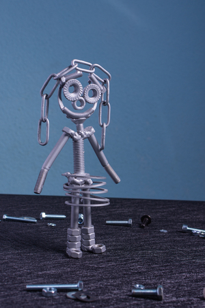 A figure of a small robot or cyborg assembled from several screws and nuts that are placed upright in textured background. It symbolizes technology, progress, engineering and industrialization.の写真素材
