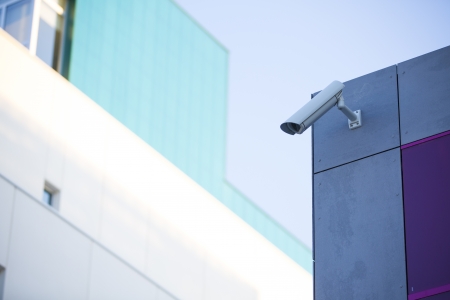 Camera system guarding blue skyscraper office building with blue sky above in horizontal formatの写真素材