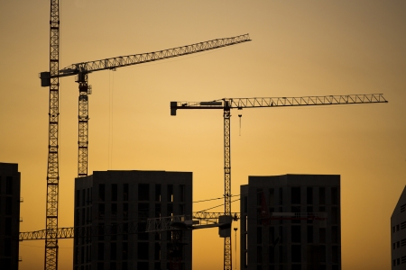 Cranes at sunset. Industrial construction cranes and building silhouettes over sun at sunrise.の写真素材