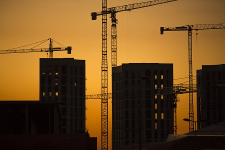 Cranes at sunset. Industrial construction cranes and building silhouettes over sun at sunrise.の写真素材
