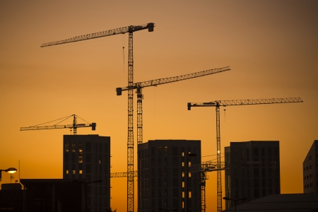 Cranes at sunset. Industrial construction cranes and building silhouettes over sun at sunrise.の写真素材