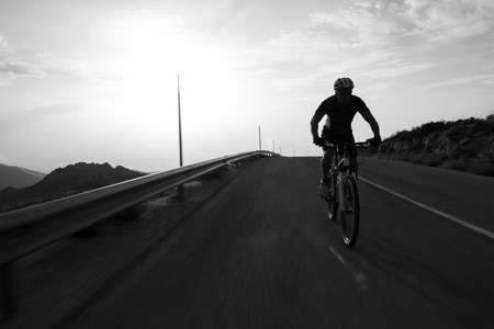 Cyclist man riding mountain on a mountain road, silhouette sunrise.の写真素材