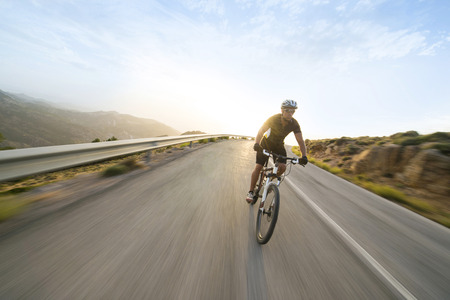 Cyclist man riding mountain bike in sunny day on a mountain road. Image with flare.の写真素材