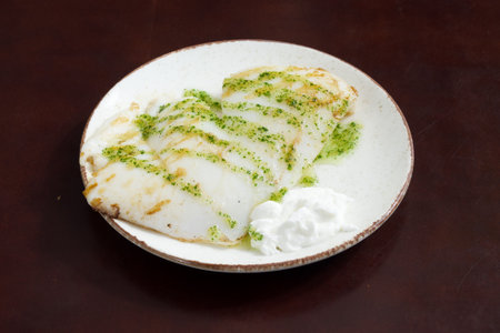 A plate of food with a white sauce and a white cream. The plate is on a wooden tableの写真素材