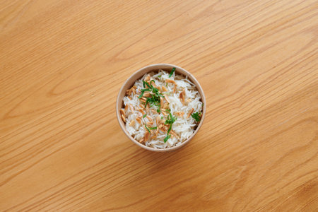 A bowl of rice with some nuts and parsley on top. The bowl is on a wooden tableの写真素材