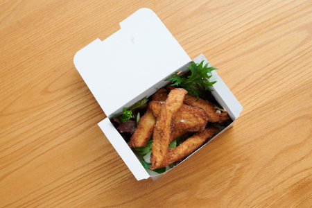 A box of fried chicken with lettuce and other vegetables. The chicken is cut into pieces. The box is...
