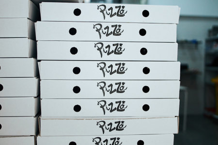 A stack of pizza boxes with the word pizza on them. The boxes are white and stacked on top of each...