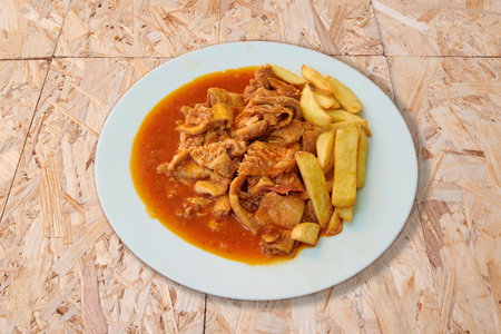 A plate of food with meat and potatoes. The meat is covered in sauce and the potatoes are cut into small piecesの写真素材