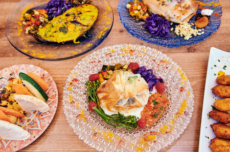 A table with a variety of food on plates. The plates are of different sizes and colors. There are also some bowls on the tableの写真素材