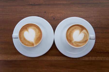 two small lattes in white cups over a wood tableの写真素材