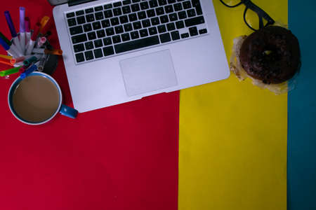 desk office with laptop, blank notepad, coffee cup chocolate donutの写真素材