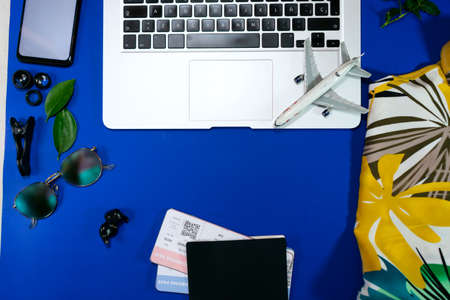 Top view essential accessories to travel concept items for trip slipper,notebook, passport, airplane,mobile phone,sunglasses on blue background.の写真素材