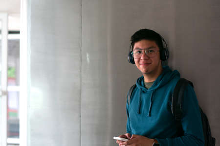 A young man watching the camera smiling and holding his smartphoneの写真素材