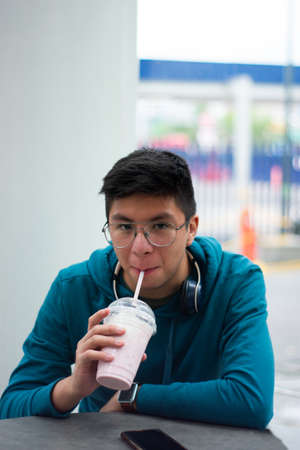 young man sips his cold beverage while looking at the camera smilingの写真素材