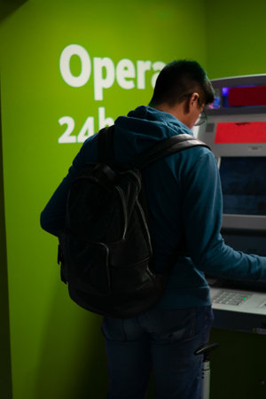 Young man using an automatic teller machine in a green office.の写真素材
