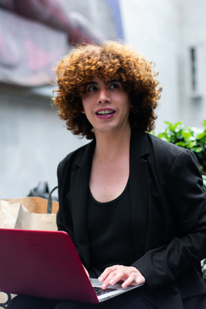 A non-binary person looking to the right working on the laptop and a paper shopping bag in the backgroundの写真素材