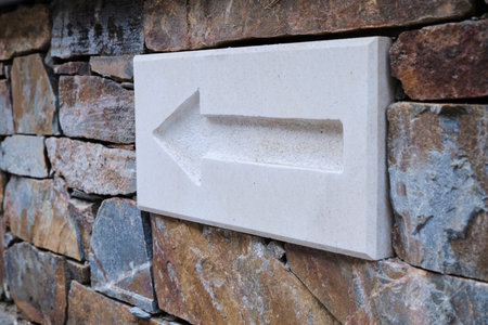 Marble panel with carved arrow installed in wall of stone building on street