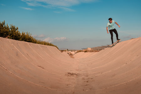 Young man wearing a blue t-shirt and black trousers skating on a tube with a blue sky and a warm atmosphereの写真素材