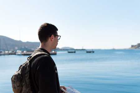 young male 20s student on his back wearing a black sweatshirt, a military backpack and glasses...