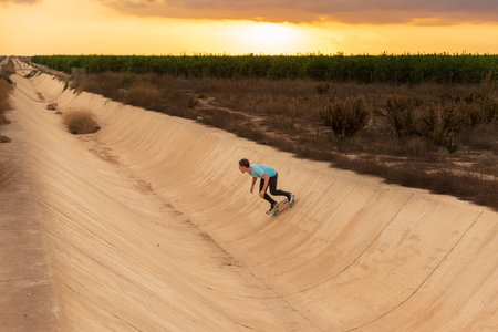 Young man wearing a blue t-shirt and black trousers skating on a tube with at sunset