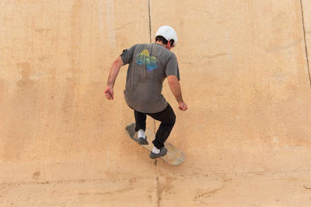 Young man skater wearing a white helmet doing a trick on a skateboardの写真素材