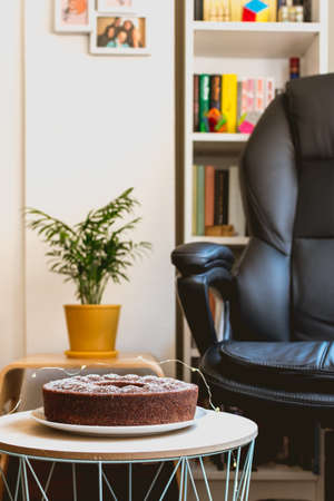 living room with a ring chocolate sponge cake, a green palm tree in a yellow pot and a black office chair with a book shelf in the backgroundの写真素材