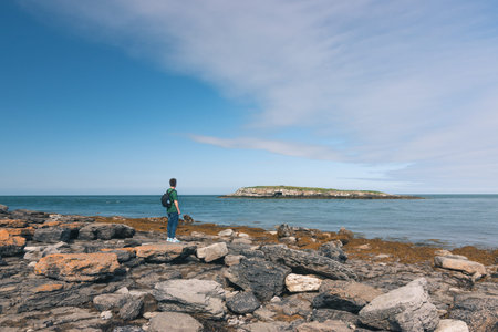 Young man adventurer wearing a green t-shirt and a backpack looking to an island in the middle of...