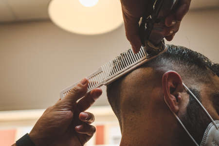 hairdresser giving a client wearing a mask a haircut with a clippers machine and a combの写真素材