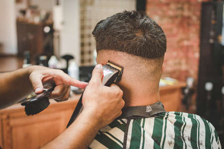 hairdresser giving a client wearing a mask a haircut with a clippers machine in a barber shopの写真素材
