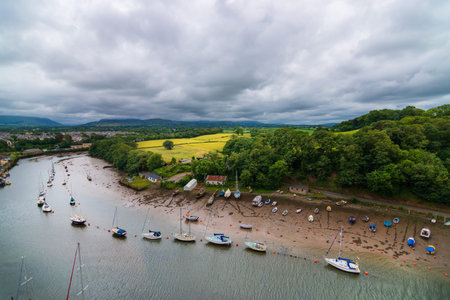 top view of boats lined up in a canal, next to a meadow, under a cloudy sky, beside Caernarfon...