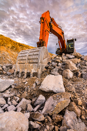 Large orange excavator in an open-pit mine, cutting stone to transform into gravelの写真素材