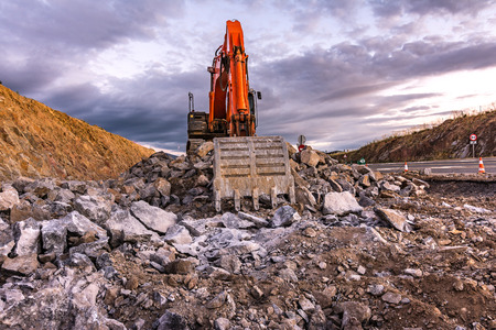 Large orange excavator in an open-pit mine, cutting stone to transform into gravelの写真素材