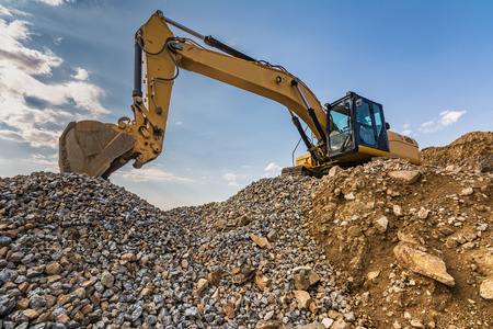 Excavator on top of a mountain of stone and sand from a quarryの写真素材