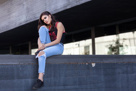 Young brunette girl sitting in fashionable pose on the street