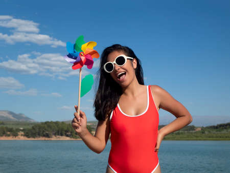 Charming shocked female in sunglasses and swimsuit standing with opened mouth against blue sky with clouds on sunny summer day in natureの写真素材