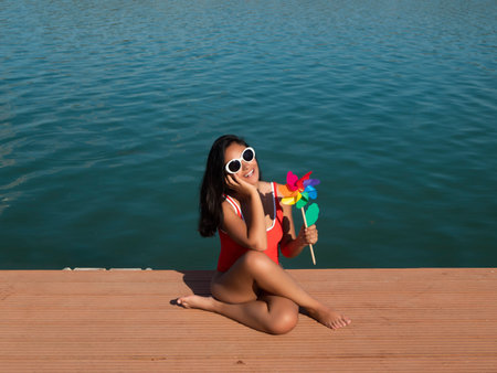 Charming shocked female in sunglasses and swimsuit standing with opened mouth against blue sky with...